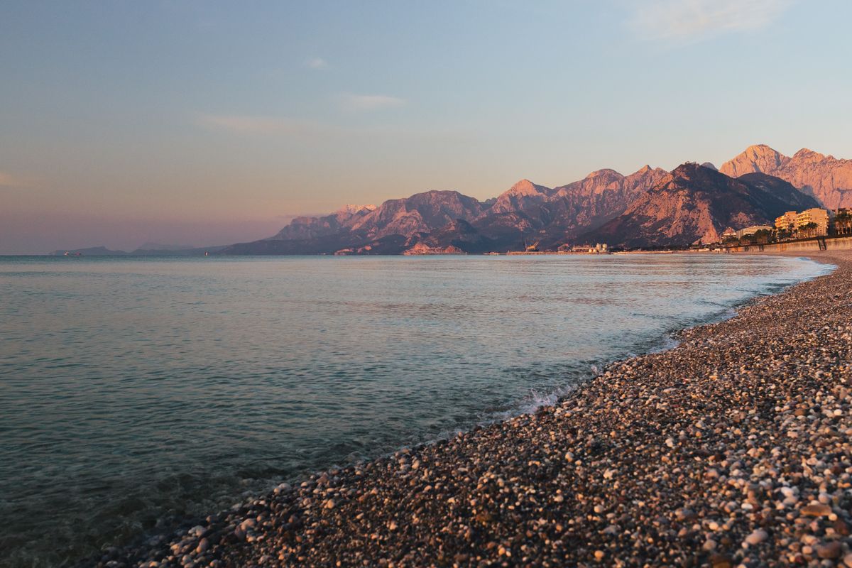 Pebble shoreline at Konyaaltı with the Beydağları mountains glowing at sunset